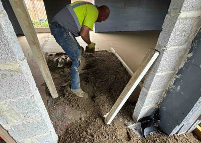 Contractor using a straight edge to accurately apply floor screed material and create a perfectly level floor surface for a home extension
