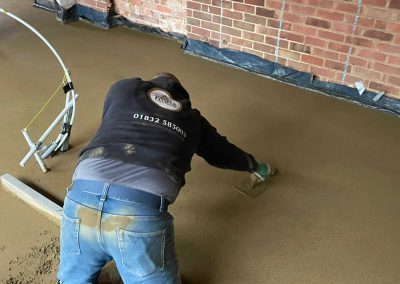 Contractor using a trowel to accurately apply floor screed material and create a perfectly level floor surface for a home extension