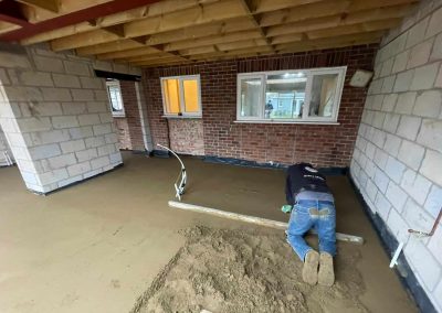 Contractor using a straight edge to accurately apply floor screed material and create a perfectly level floor surface for a home extension