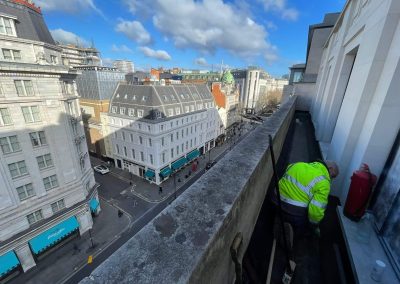Worker installing floor screed onto a narrow ledge, high up over London, with view down onto a busy London street
