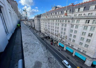 Worker installing floor screed onto a narrow ledge, high up over London, with view down onto a busy London street