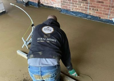 Contractor using a straight edge to accurately apply floor screed material and create a perfectly level floor surface for a home extension