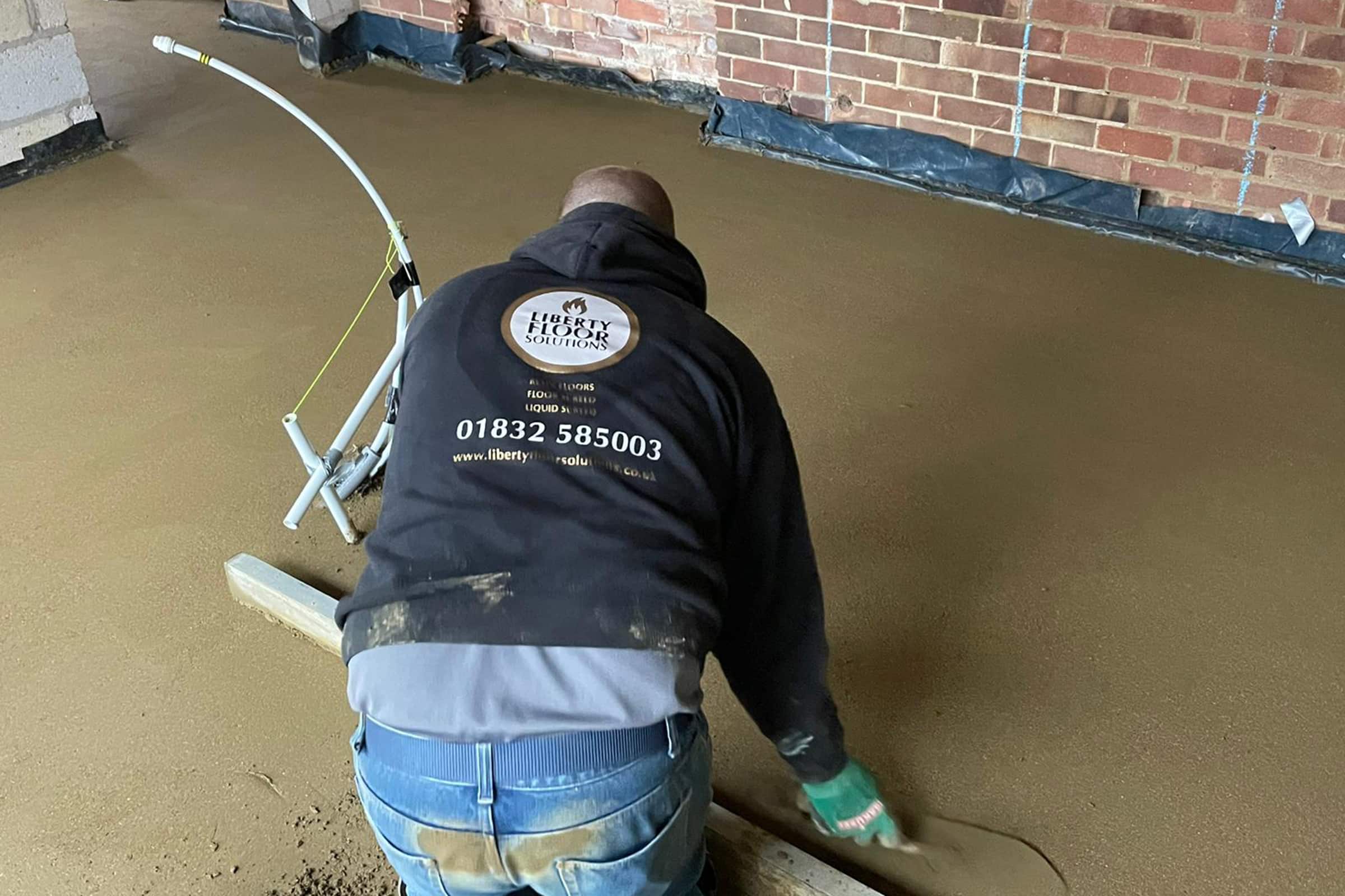 Contractor using a straight edge to accurately apply floor screed material and create a perfectly level floor surface for a home extension