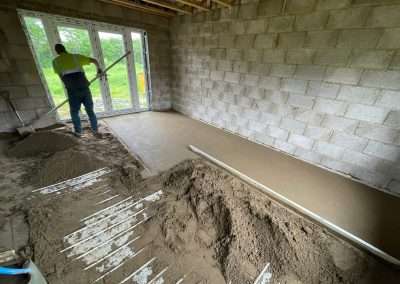 Contractor using a straight edge to accurately apply floor screed material and create a perfectly level floor surface for a home extension