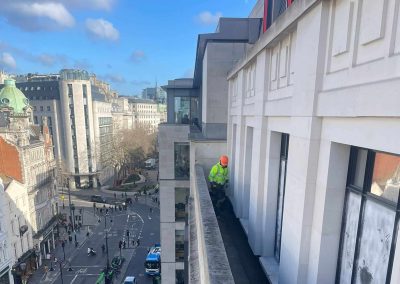 Worker installing floor screed onto a narrow ledge, high up over London, with view down onto a busy London street