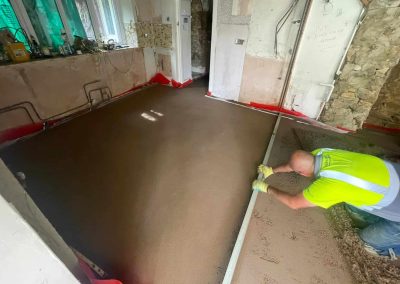 Contractor using a straight edge to accurately apply floor screed material and create a perfectly level floor surface for a home extension