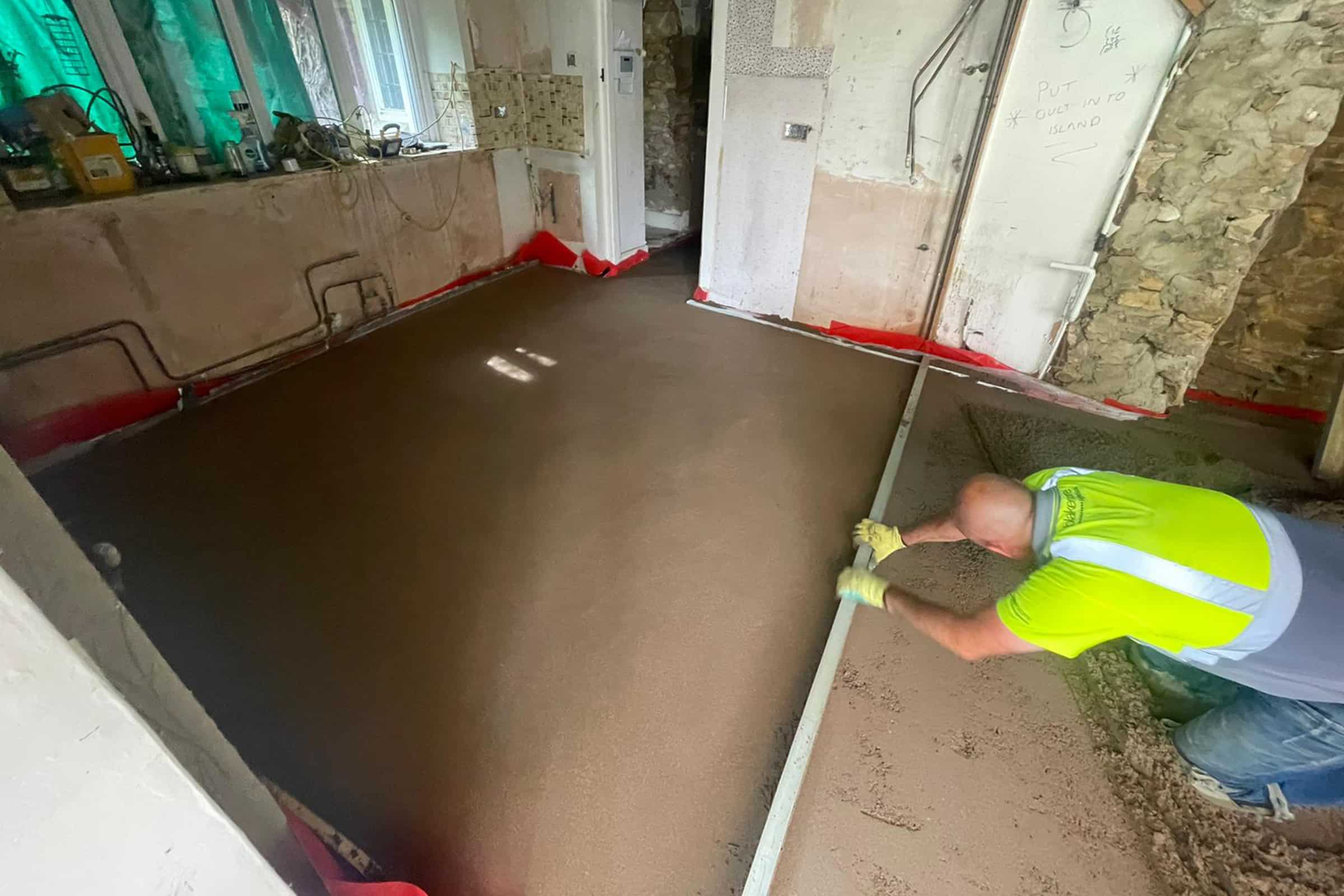 Contractor using a straight edge to accurately apply floor screed material and create a perfectly level floor surface for a home extension