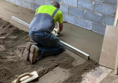 Contractor using a straight edge to accurately apply floor screed material and create a perfectly level floor surface