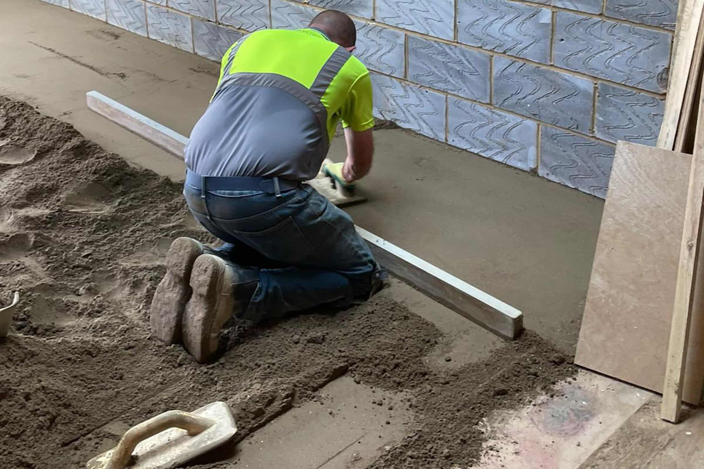 Contractor using a straight edge to accurately apply floor screed material and create a perfectly level floor surface