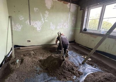 Contractor using a straight edge to accurately apply floor screed material and create a perfectly level floor surface for a home extension