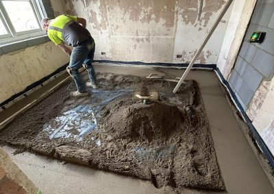 Contractor using a straight edge to accurately apply floor screed material and create a perfectly level floor surface for a home extension