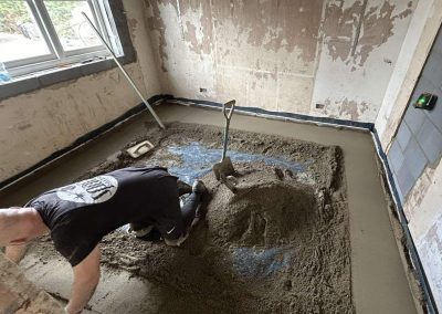 Contractor using a straight edge to accurately apply floor screed material and create a perfectly level floor surface for a home extension