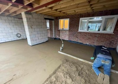 Contractor using a straight edge to accurately apply floor screed material and create a perfectly level floor surface for a home extension